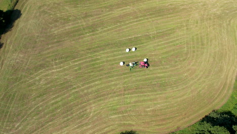 Top-down-aerial---farmer-collects-grass-bales-from-meadow---mechanized-agriculture-with-advanced-machinery-and-modern-tractors