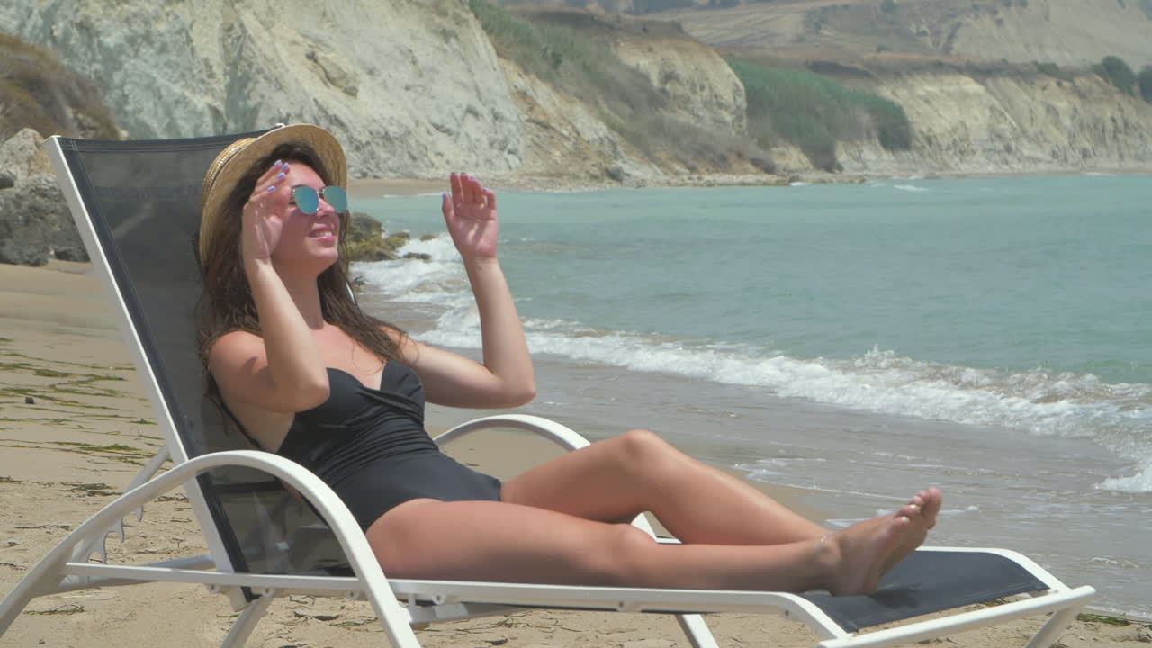 A young woman in a bikini relaxes on a beach chair, enjoying the sun and the ocean.