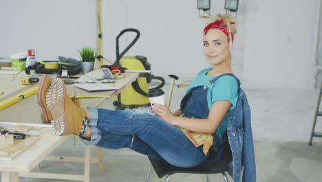 female relaxing at carpenter workbench with drink