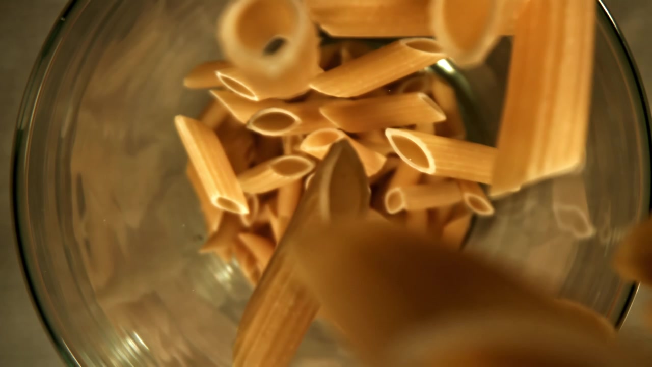 Penne crude che cadono al rallentatore in una ciotola di vetro