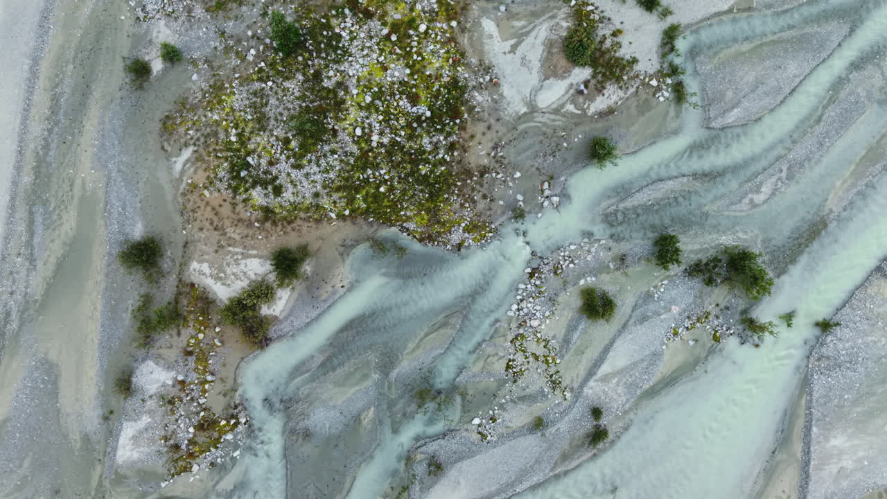 Drone orbits and descends in top-down view over braided glacial river channels