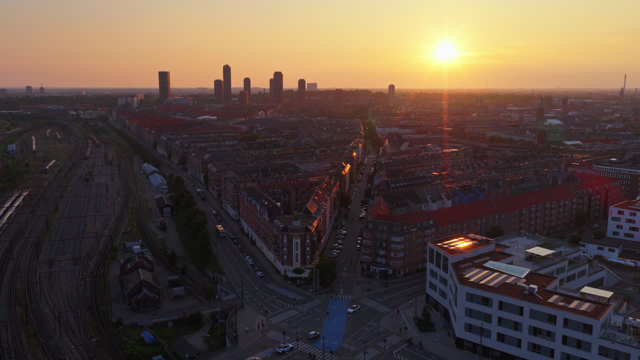 Aerial drone view of railway lines and rooftops in Vesterbro with the sun setting behind modern towers in Copenhagen, Denmark