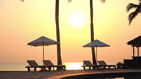 two sun umbrella and four deckchairs poolside with sea in background at sunset