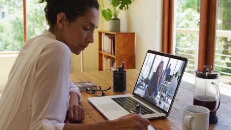 Mixed-race-businesswoman-sitting-at-desk-using-laptop-having-video-call-with-female-colleague