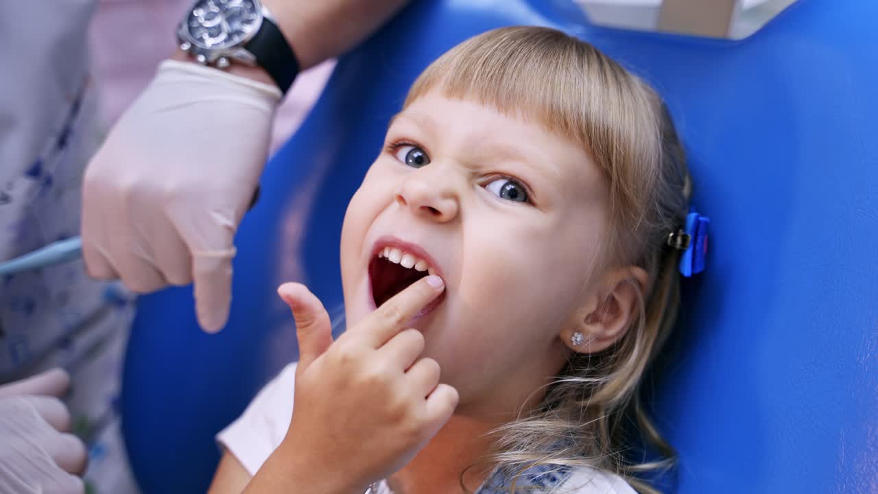 Little child in stomatology chair points at the ill tooth with a finger - close up video. Healthy teeth concept video.