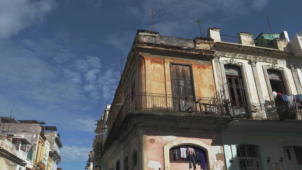 Una vista dal basso cattura una facciata angolare coloniale invecchiata all'Avana, Cuba, con balconi in ferro, vernice scrostata, bucato steso e un cielo blu intenso, per temi di architettura urbana sotto il sole all'aperto.