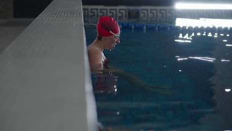 una mujer con una gorra de natación roja y gafas se está preparando para nadar en una piscina.