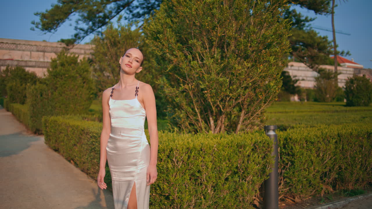 녹색 헤지 골목을 걸어다니는 여자 카메라를 보고. 아름다운 정원을 산책하는 소녀