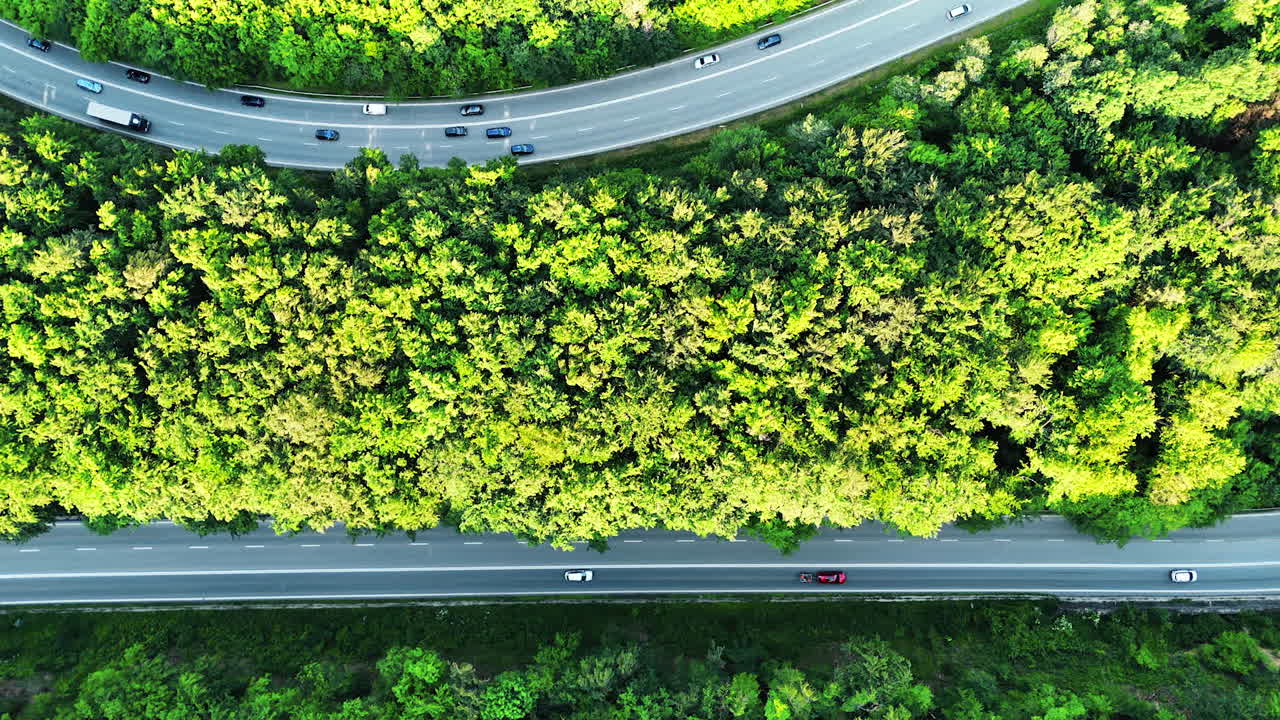 Two roads with cars moving by. Wooded countryside crossed by the highways. Top view