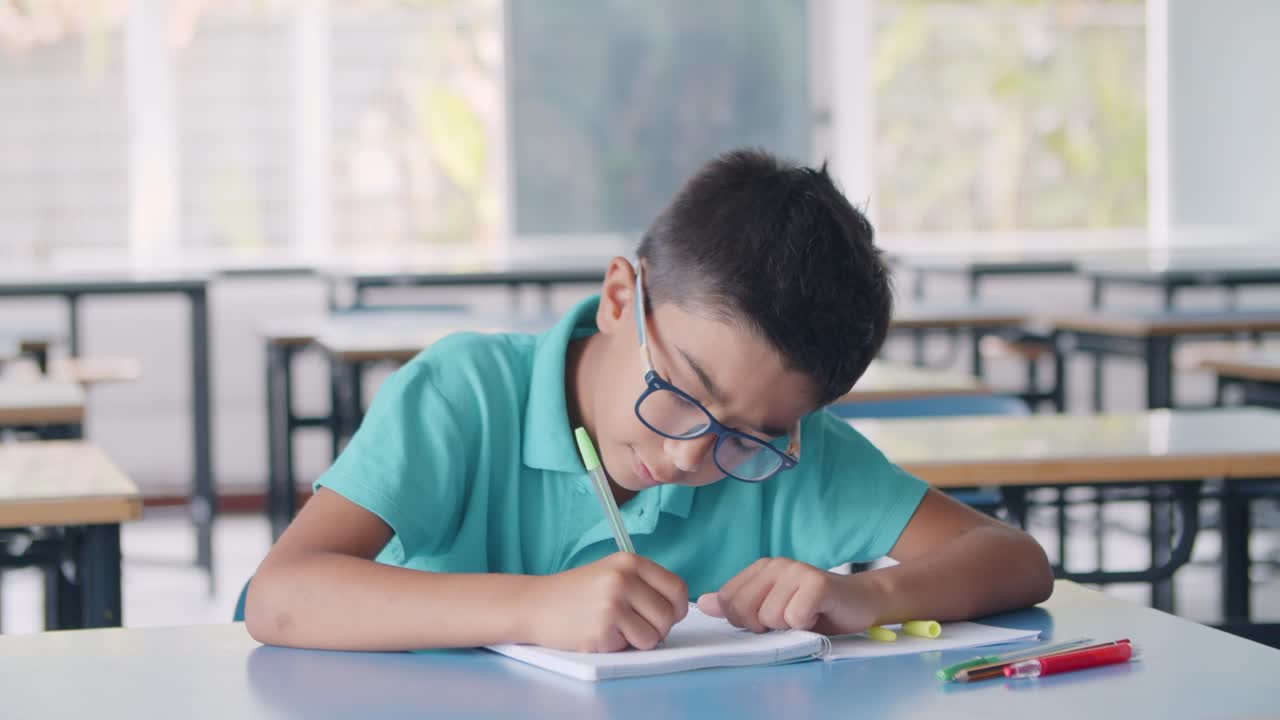 Focused Hispanic pupil boy wearing glasses and doing homework