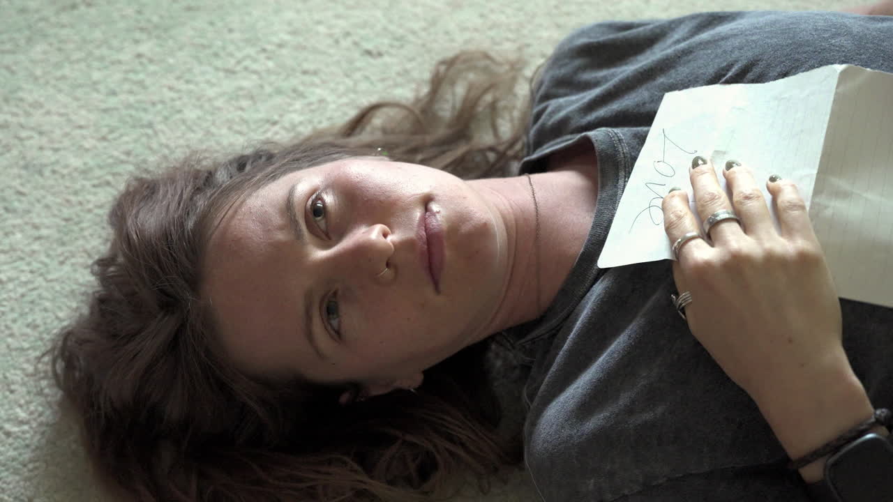 A woman lies on the ground reading a love letter, then closes her eyes and clutches it to her chest, embracing the emotions as she savors the heartfelt words