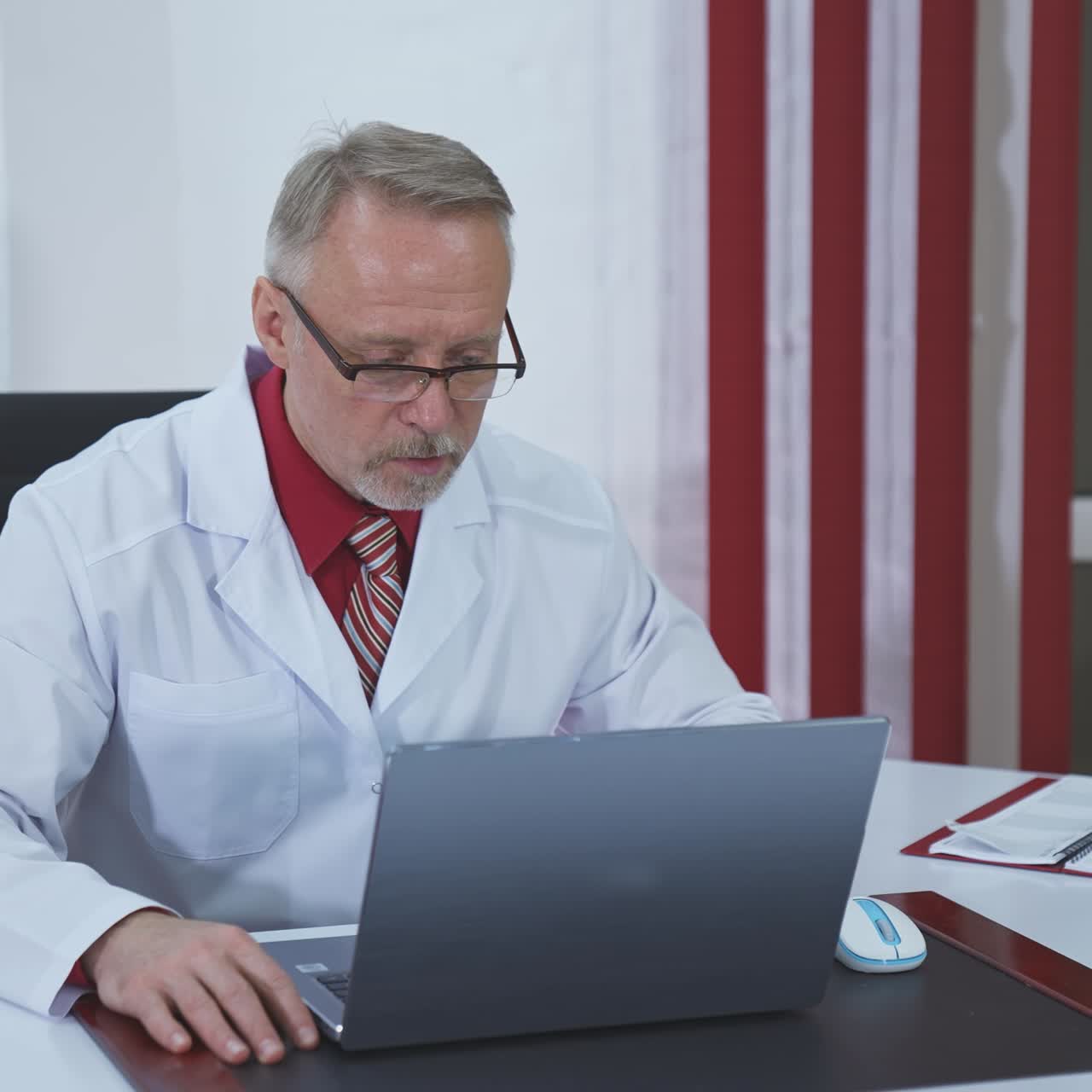Older doctor making video call on laptop. Senior male physician talking to patient while looking at pc screen communicating by webcam in web chat. Telemedicine concept.