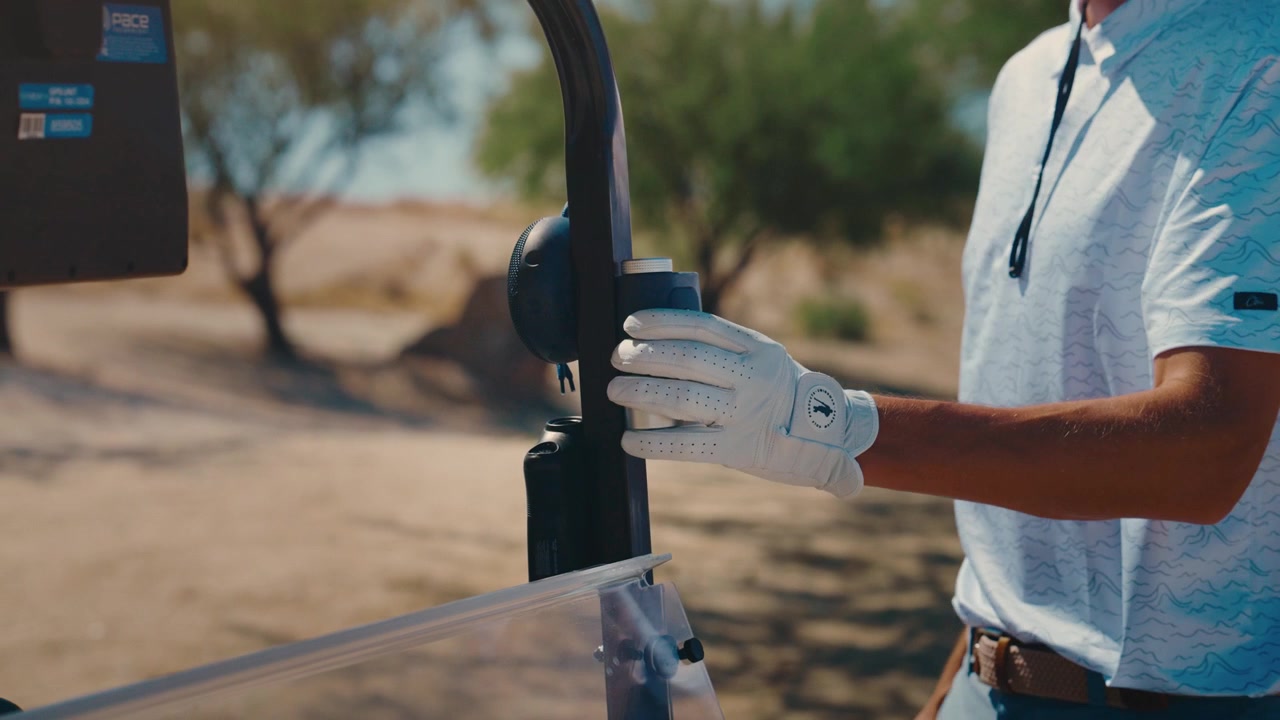 Un golfista posiziona il magnete del telemetro sul golf cart, primo piano su un campo soleggiato nel deserto, al rallentatore.
