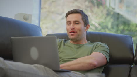 relaxed man wearing pyjamas lying on sofa at home making video call on laptop- shot in slow motion