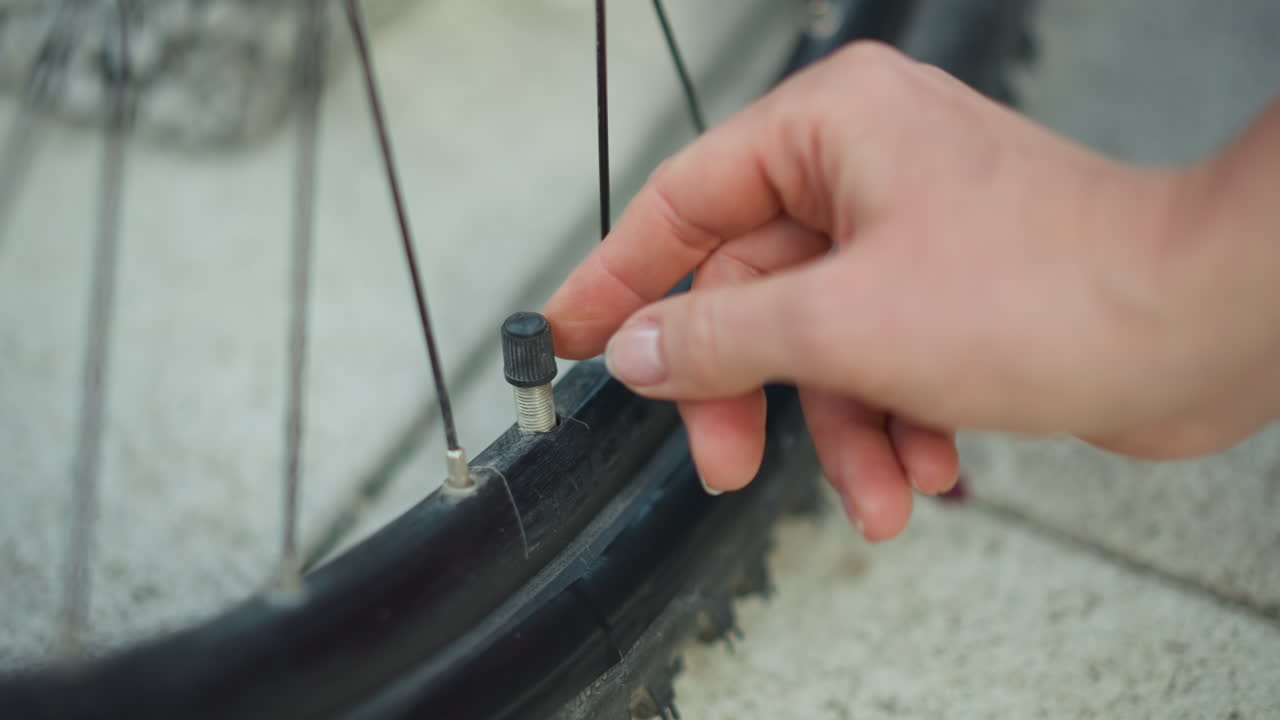 Nærbillede af en kvindes hænder, der monterer en ventildæksel på et cykeldæk før weekendturen, detaljeret fælg og eger, afslappet hobbyrytter og bybud, der tjekker pumpe og slange, sollys glimter på metal, stemning.