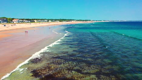 drone view shows crowds on saco, maine’s beaches. tourists relax, kids splash in waves, houses stand along the shore. peak-season east coast vibe with ocean, sand, and coastal new england charm