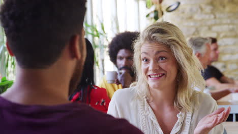 young adult woman talking to her boyfriend at a table in a busy restaurant during the day, over shoulder view