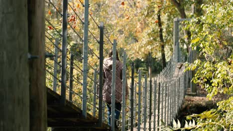 Girl-in-a-purple-warm-cozy-jacket-walks-across-a-suspension-bridge-during-the-autumn-season