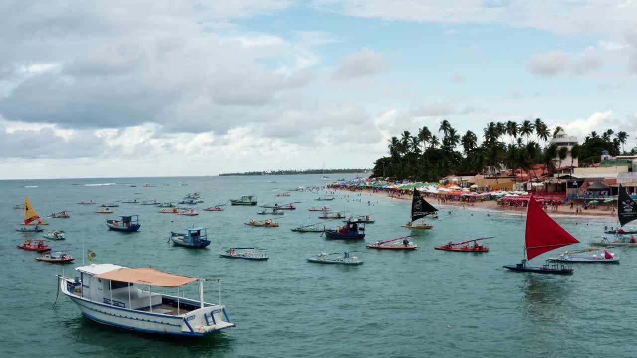 toma aérea con drones de la playa porto de galinhas o puerto de pollo con veleros anclados, sombrillas coloridas y turistas nadando en el agua cristalina del océano en pernambuco, brasil