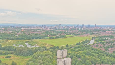the area near salford city fc shows residential tower blocks, green parkland, and the manchester skyline on the horizon, captured in a slow drone glide