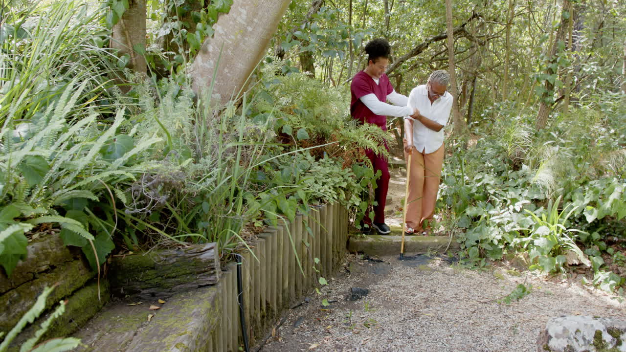 Caregiver assisting senior woman walking with cane in peaceful garden setting, copy space
