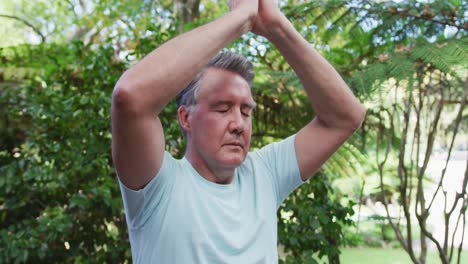 hombre caucásico mayor practicando yoga sentado en posición de loto estirándose y meditando en el jardín