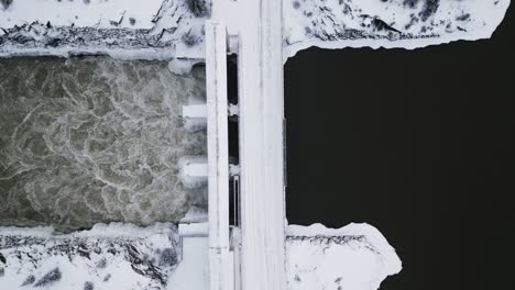 Close-Up-Slow-Establishing-Shot-Aerial-Drone-View-Rushing-Water-Notigi-Hydro-Dam-River-Snowy-Landscape-Northern-Winter-Manitoba-Canada