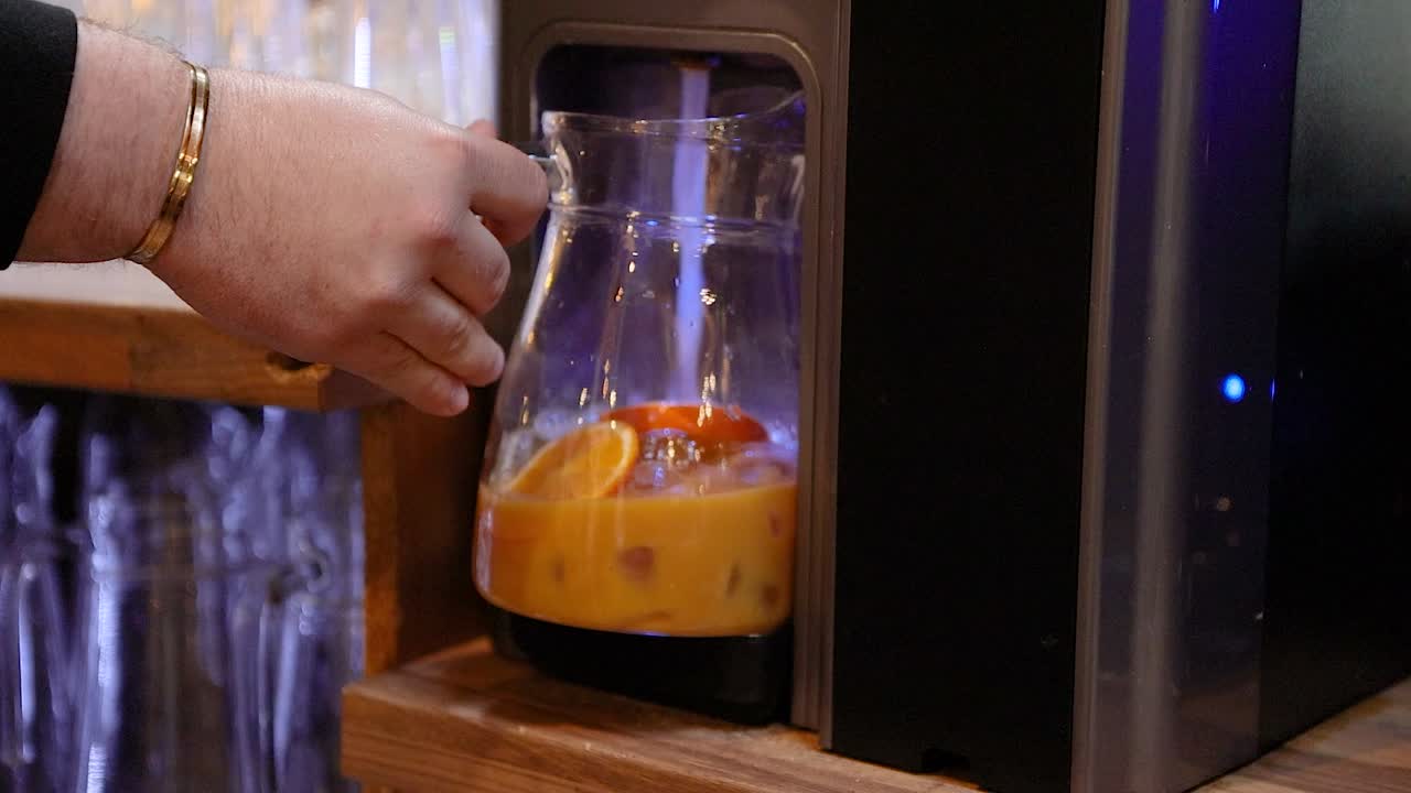 Un camarero barista preparando una limonada añadiendo agua con gas a la jarra con fruta y sirope