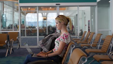 young woman working on laptop at airport waiting area, casual attire, tranquil atmosphere