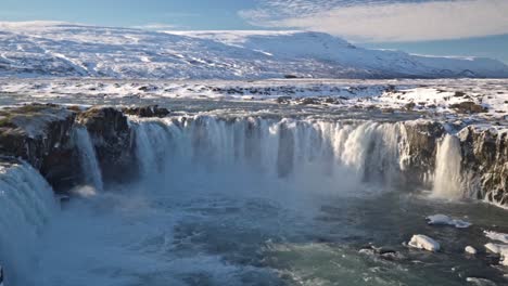 a powerful torrent of water plunges over goðafoss, iceland's "waterfall of the gods," set against a stunning winter landscape, framed by snow-covered rocks and icy formations