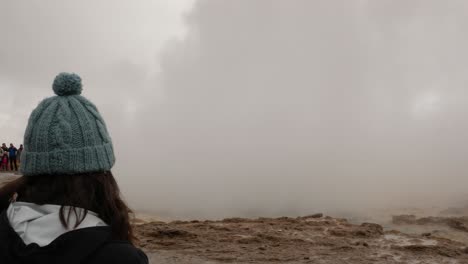 una mujer joven frente a un geyser en islandia.