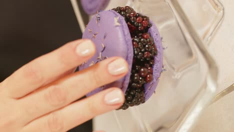 close up of purple colored macarons with blueberry in the middle in glass container on the table