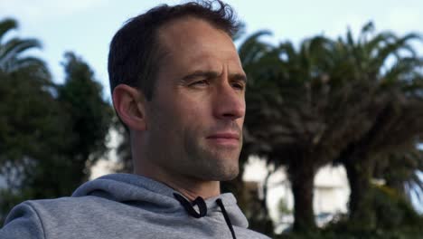 Close-up-of-young-caucasian-man-drinking-coffee-sitting-on-a-bench-at-the-beach-in-Auckland,-New-Zealand