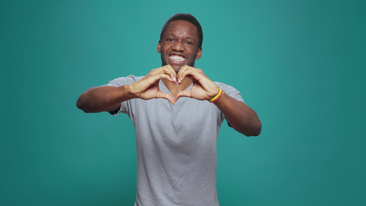 Uomo sorridente che fa un cuore con le mani davanti alla fotocamera