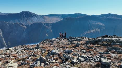 two couples stand on cliff discussing and pointing at landscape. drone circles behind, creating a parallax effect with fjord and mountains
