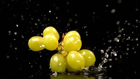 Green-grapes-falling-on-water-against-black-background-4k