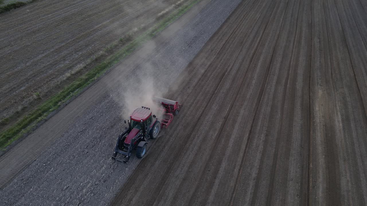 Low-altitude drone view of tractor plowing straight lines across farmland. Perfect symmetry of soil patterns on autumn day