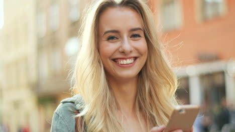 close-up view of young blonde woman texting on her smartphone and looking at the camera in the street