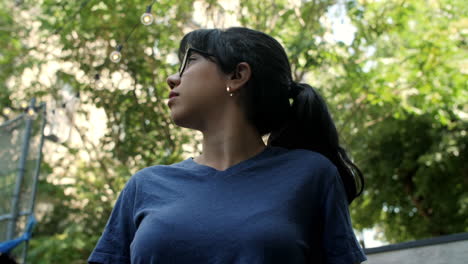 a young latina woman wearing glasses looks up to the sky and trees on a sunny day