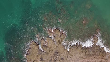 High-Ascending-Shot-Of-Rocks-At-The-Shoreline-With-The-Waves-Going-Over-The-Top