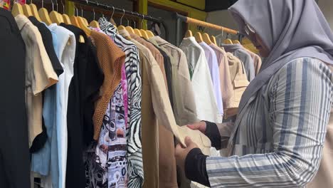 muslim woman choosing clothes on hanger at clothing store