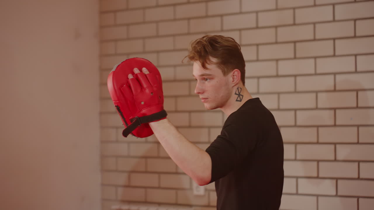 Boxer wearing red training pads practices sparring session with focus and determination, preparing for combat through drills, showcasing athletic skill, discipline, power, endurance in indoor gym environment