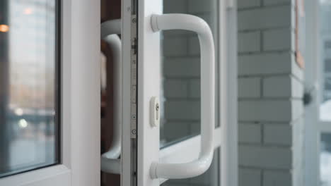 close up of young woman in ribbed white sweater opening glass door while entering mall, capturing gentle grip on curved white handle with natural daylight and blurred reflections in background