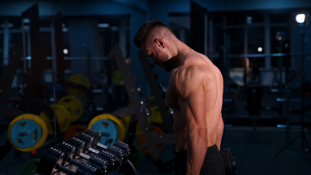 Bodybuilder muscoloso che tiene i manubri. Giovane uomo in forma che tiene i manubri mentre si allena in palestra