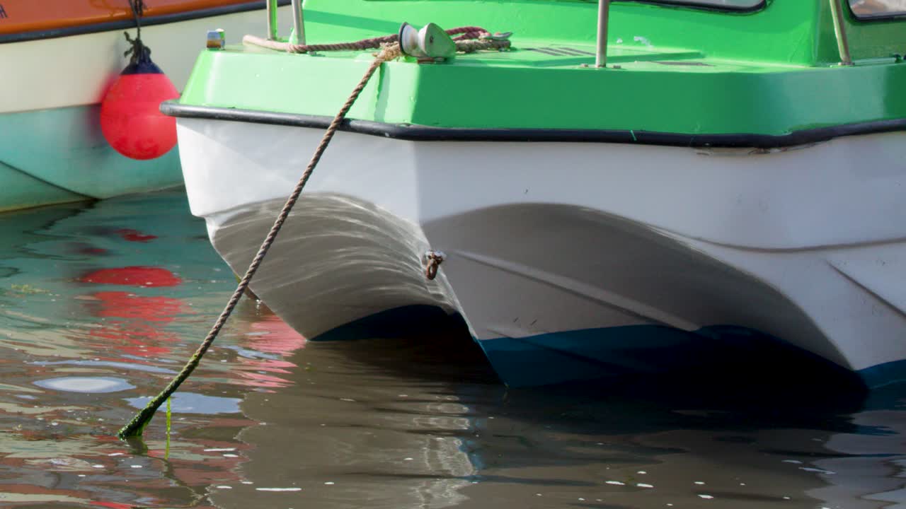 Close-up of green and white motorboat floating, moored, with subtle movement in bright daylight