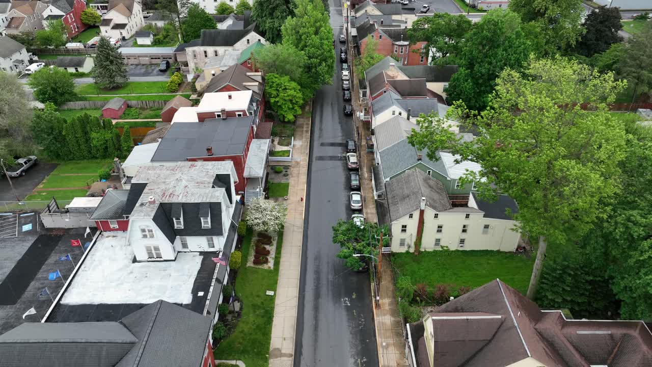 Waving american flag on flagpole of front yard. Aerial descend wide shot. Street of patriotic american neighborhood in Spring season. Rooftops of row homes in Pennsylvania, United States. Proud nation