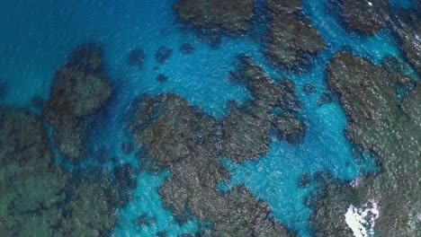 a drone captures a shot of a blue lagoon, showcasing the crystal-clear waters that you can see the rocks and the bottom of the sea, offering a glimpse of the natural beauty of the underwater world