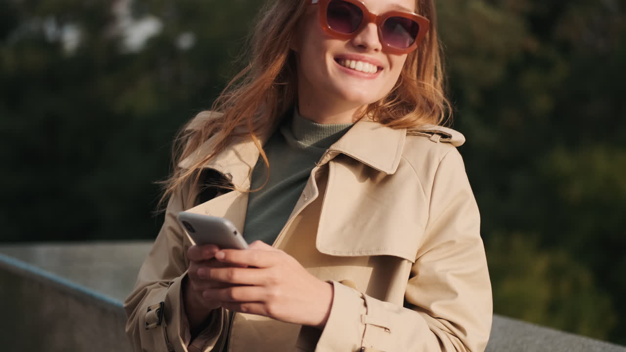 кавказская студентка использует смартфон и улыбается на открытом воздухе.