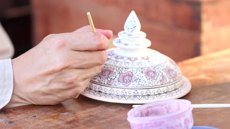 artist carefully painting traditional thai bowl at outdoor workshop