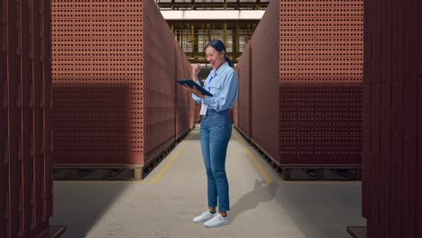 full body side view of asian female with her tablet with red brick packed in stacks are stored, she raises her fist up with screaming goal
